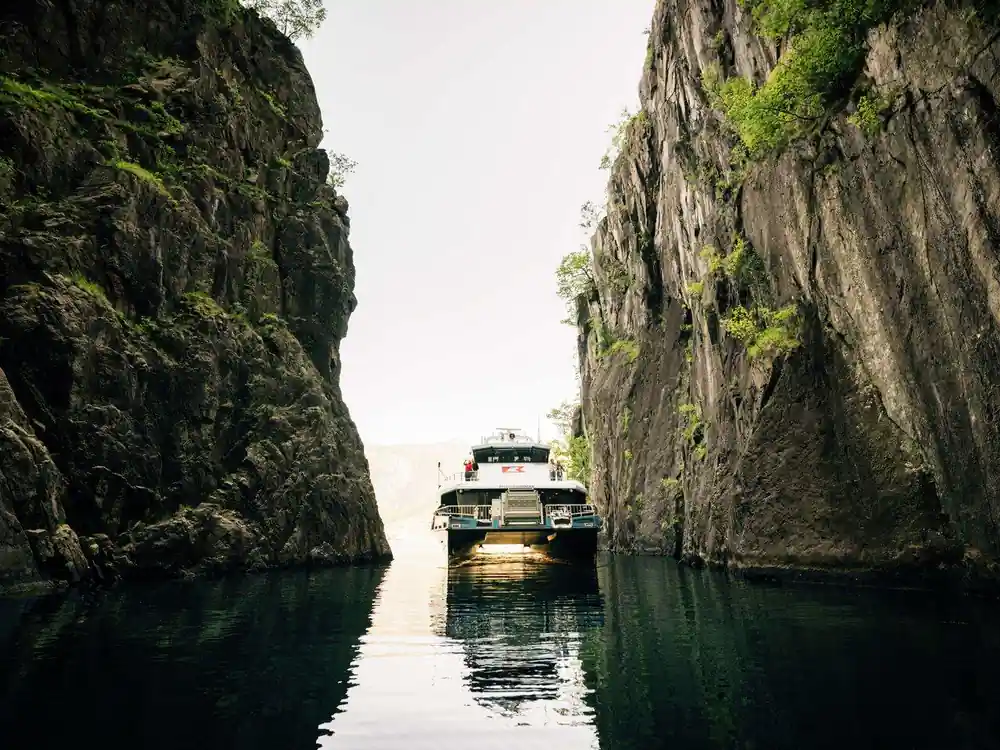 Boat traveling through narrow channel between tall rock cliffs