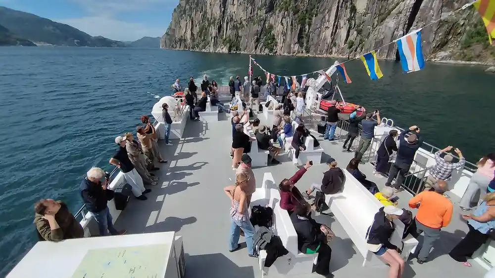 Crowded tourist boat deck with people and mountain cliffs