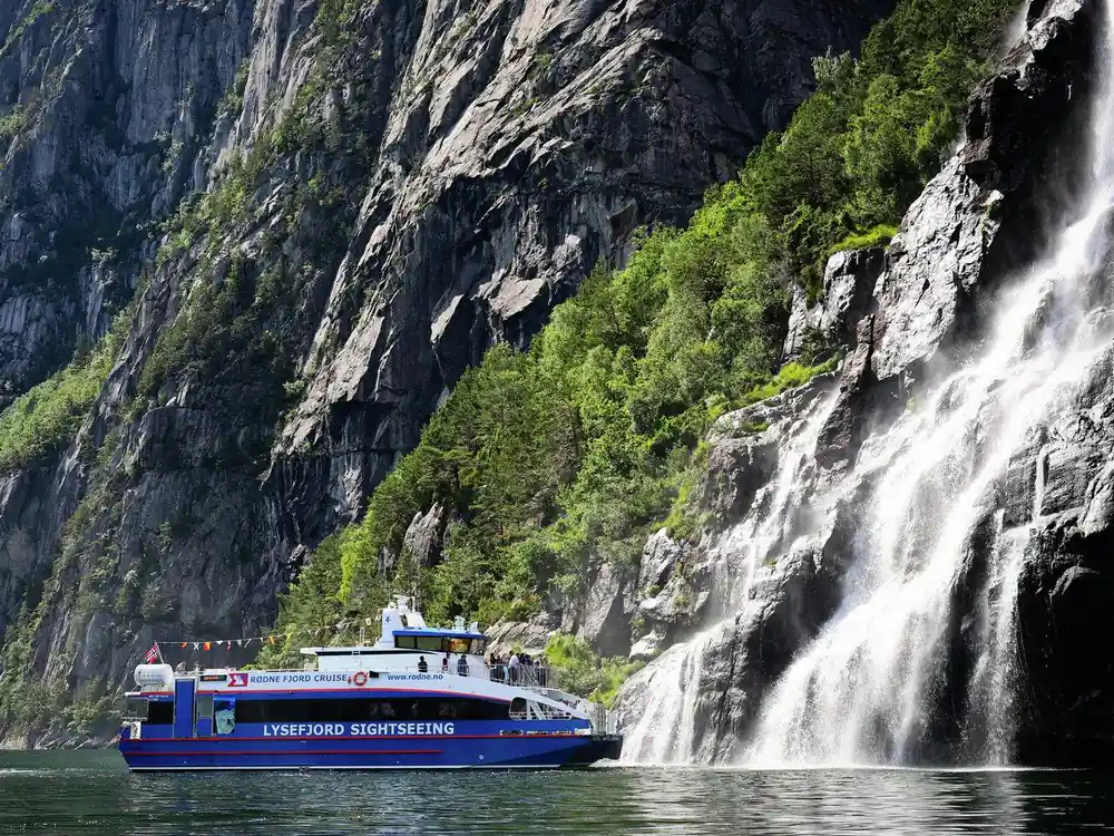 Large waterfall cascading down cliff beside sightseeing boat