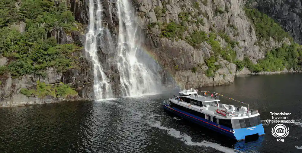 Large waterfall cascading into fjord beside passing boat