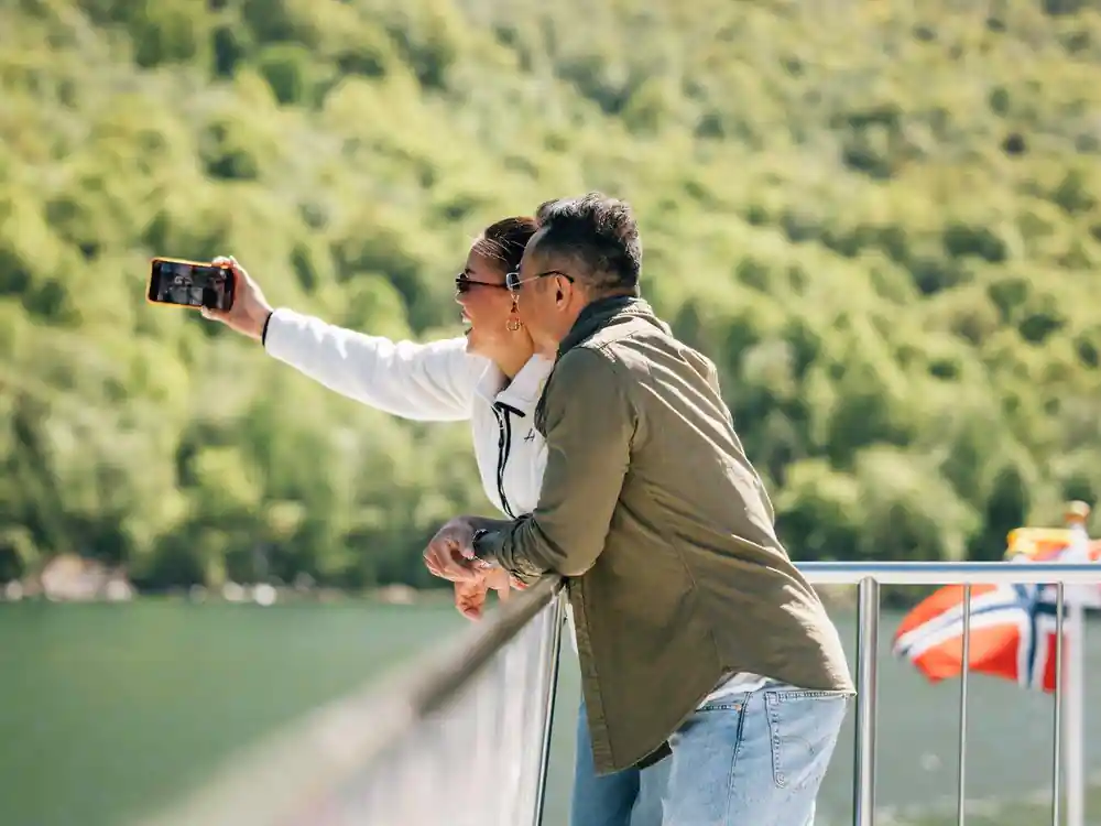 Man taking selfie on boat deck near green water and mountains