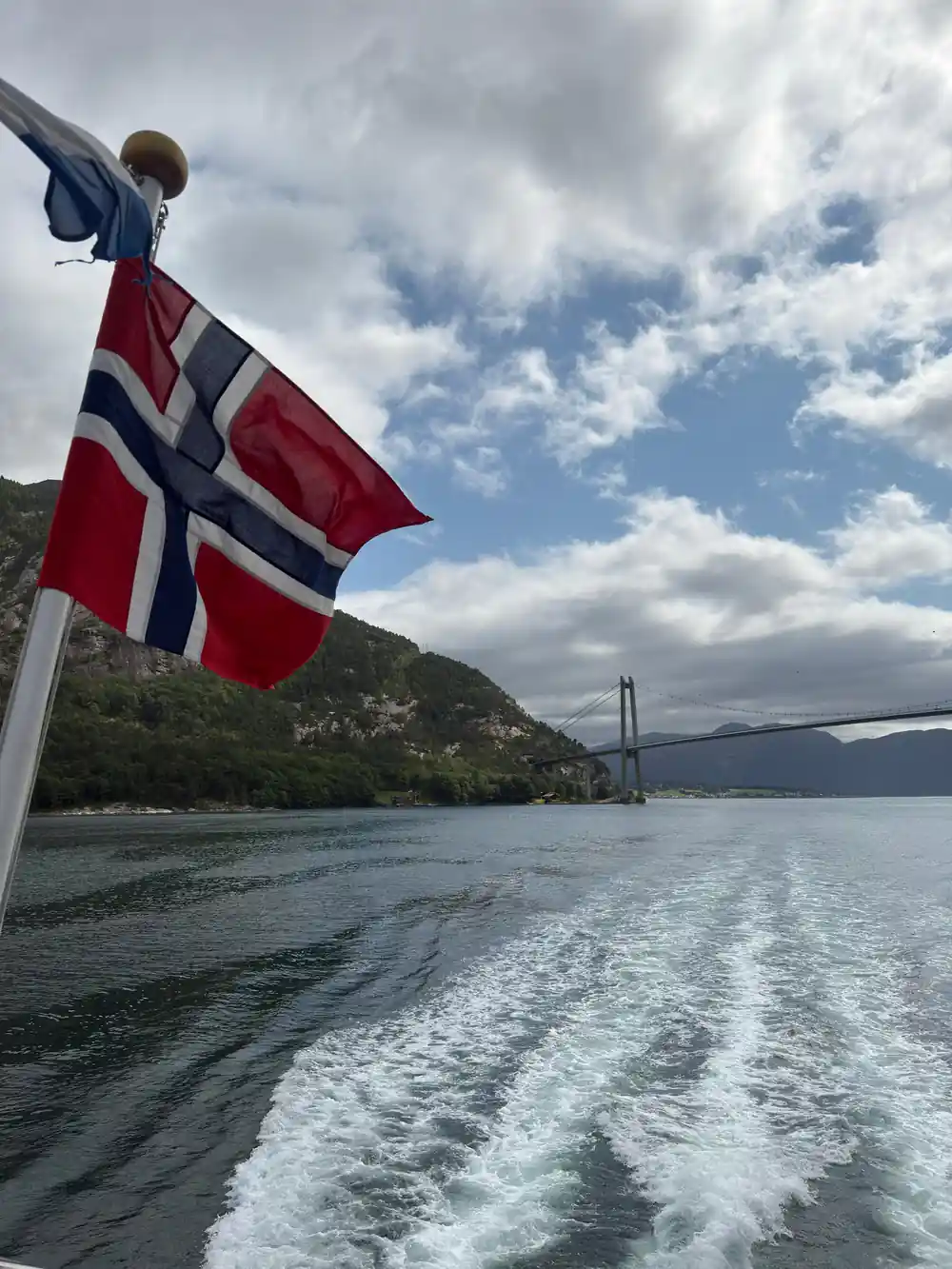 Norwegian flag on boat with bridge and mountains