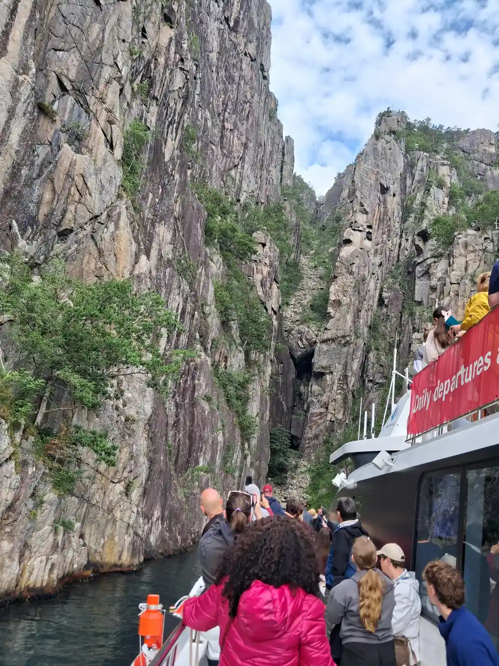 Passenger boat with crowd navigating narrow rocky fjord