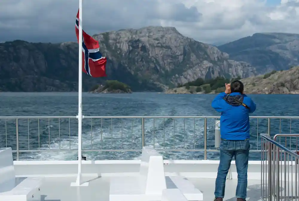 Person on boat deck with Norwegian flag and mountain backdrop