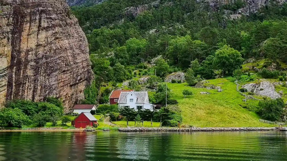 Red wooden house on grassy hillside below tall rock cliff