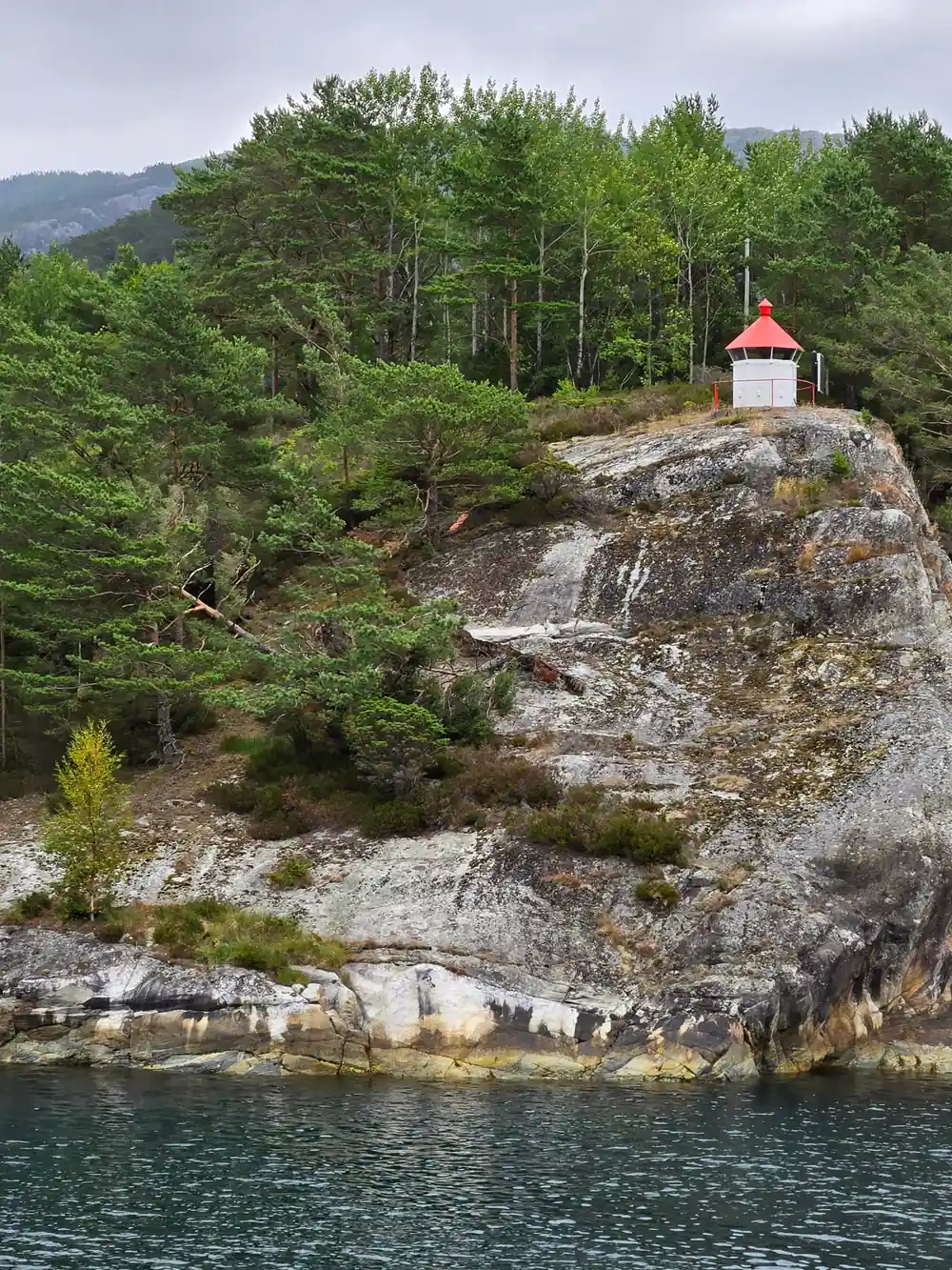 Small chapel on rocky outcrop above forested waterside