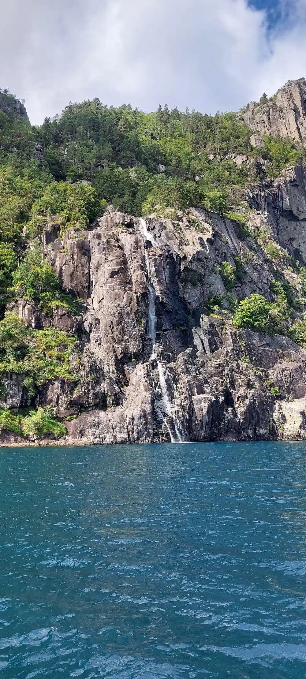 Steep rocky mountain cliff rising from green fjord water
