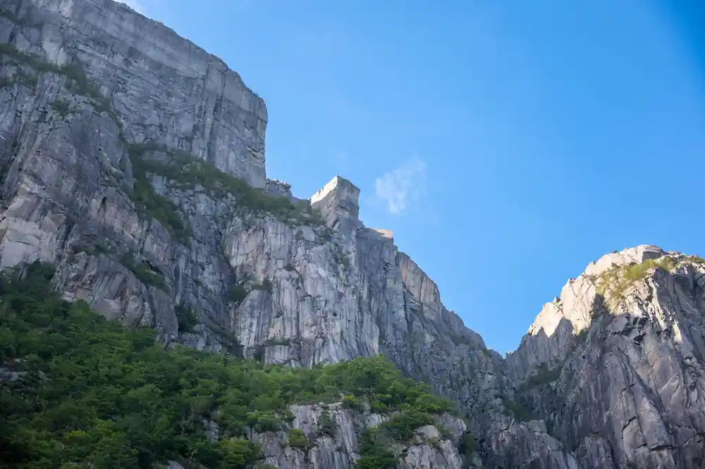 Tall rocky cliff face with small building structure at summit