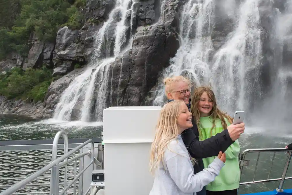 Three people on boat deck viewing large waterfall on cliff face