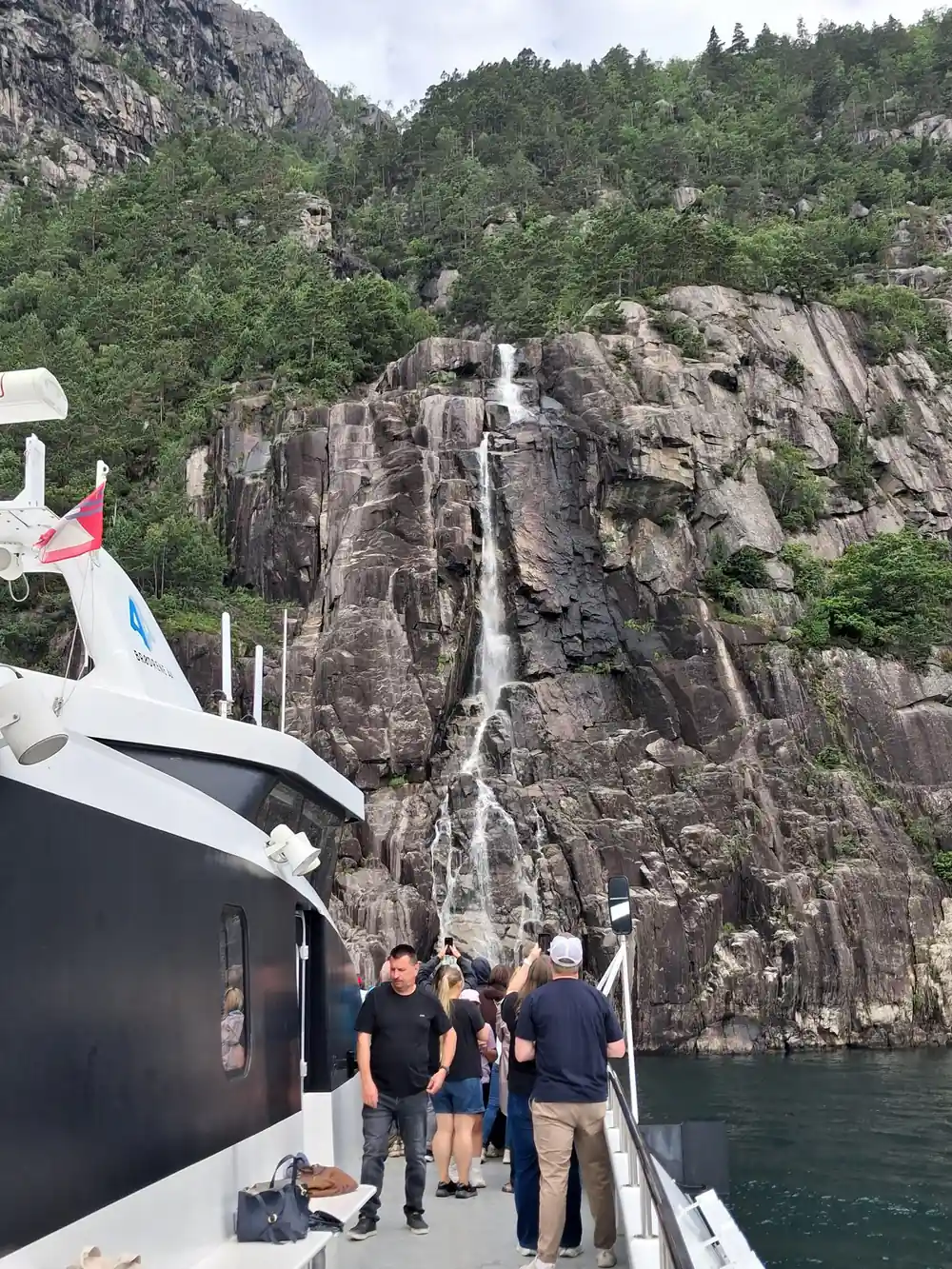 Tour boat with passengers near tall waterfall on cliff