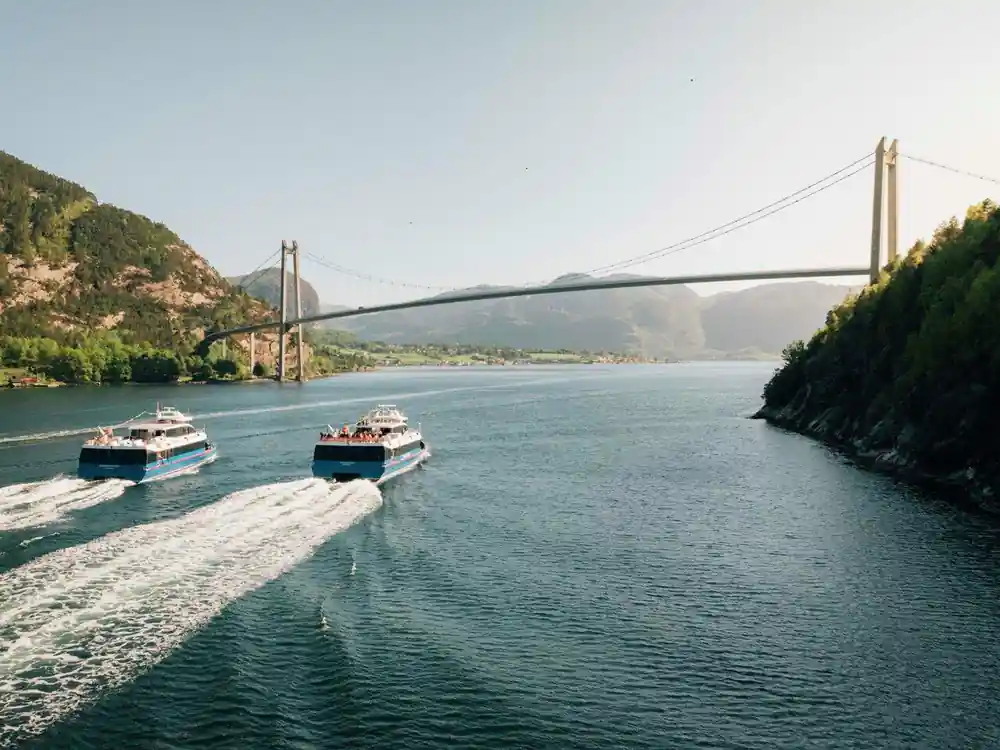 Two ferries on water under suspension bridge and mountains