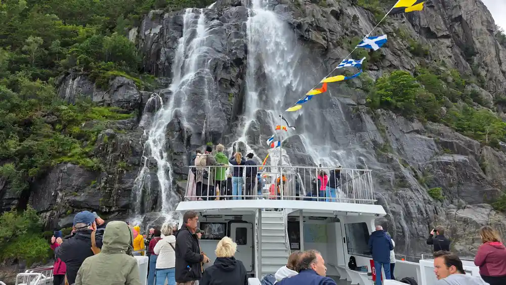 Waterfall cascading down rocky cliff with tour boat below