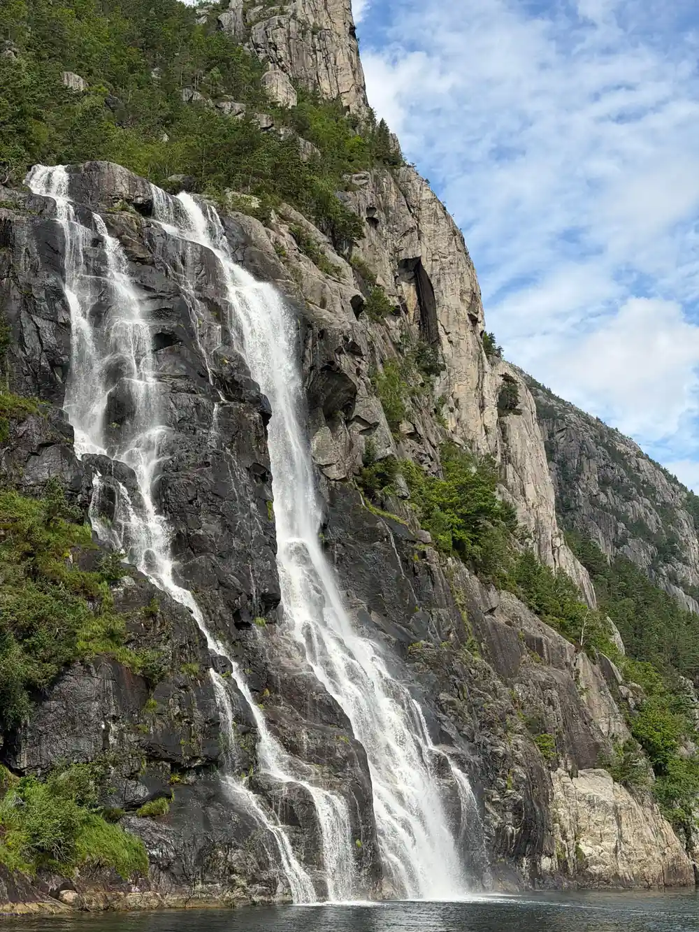 Waterfall cascading down steep rocky cliff into fjord